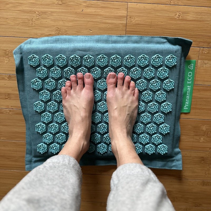 A pair of feet standing on a Pranamat acupressure mat that stimulates the nerves of the feet
