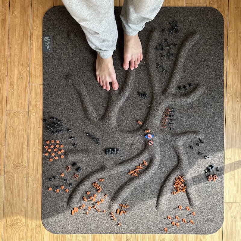 A pair of feet standing on a brown Rooty Rug that has uneven floor texture to stimulate the feet