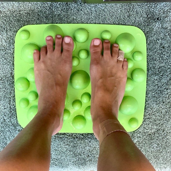 A pair of feet standing on Xero Shoes Rox mat - a floor mat for foot texture input.