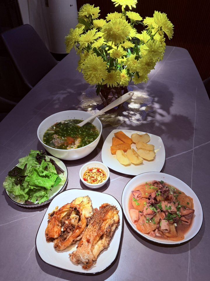 Mâm cơm dân dã nhưng hấp dẫn với món cá rán giòn, mực xào, canh cá, rau sống ăn kèm nước mắm tỏi ớt và tráng miệng với đĩa trái cây. Bữa ăn giản dị, mộc mạc mà ấm lòng, đầy hương vị từ ký ức tuổi thơ.